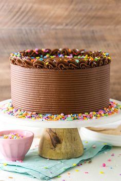 a chocolate cake with sprinkles sitting on top of a white plate next to a pink bowl