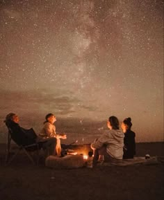 three people sitting around a campfire under the night sky