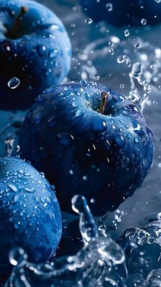 three blue apples with water splashing on them