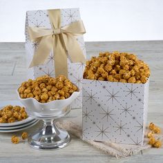 two white bowls filled with caramel popcorn next to a gift box on a table