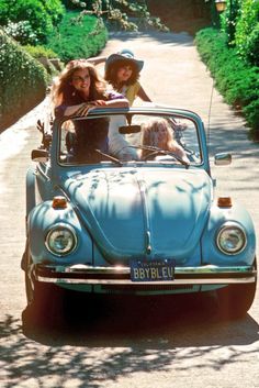 two women are riding in the back of an old vw beetle on a dirt road