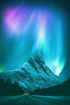 the aurora bore is shining brightly in the night sky over a snowy mountain and road