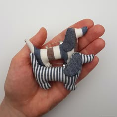 a hand holding a small blue and white striped dog brooch with its tail curled up