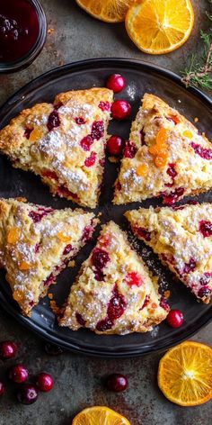 slices of cranberry orange scones on a black plate surrounded by oranges and cranberries