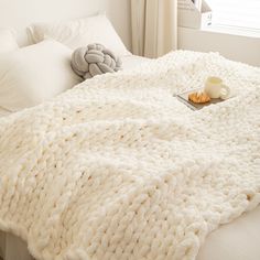 a white blanket on top of a bed next to pillows and a tray with food