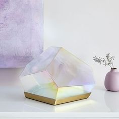 a white vase sitting on top of a table next to a purple vase with flowers in it