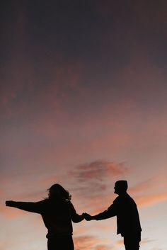 two people holding hands while standing on top of a hill under a pink and blue sky