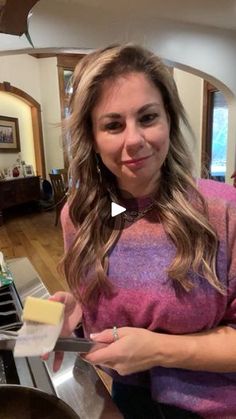 a woman standing in front of a stove holding a piece of butter and looking at the camera