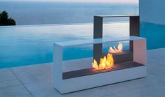 an outdoor fire pit sitting on top of a patio next to a swimming pool with the ocean in the background