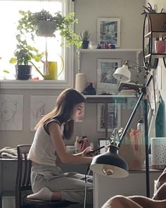 a woman sitting on a chair in front of a desk with a lamp above it