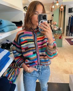 a woman is taking a selfie in the mirror while wearing a multicolored jacket