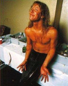 a man with long hair and no shirt standing in front of a sink