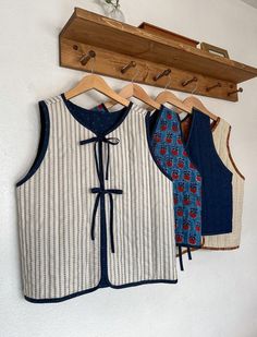 three vests hanging up on a wall with wooden hangers and clothes pins attached to them