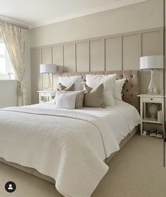 a white bed sitting in a bedroom next to a window with drapes on it