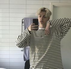 a young man taking a selfie in the bathroom with his cell phone while wearing a striped shirt