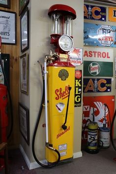 a yellow shell gas pump sitting next to a wall filled with signs