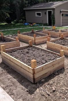 several wooden raised garden beds with dirt on the ground in front of a house and trees