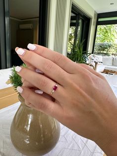 a woman's hand with white and pink manicured nails holding a small vase