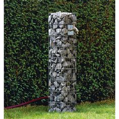 a tall metal pole sitting in the grass next to a hedge covered with rocks and stones