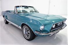 an old blue mustang convertible car parked in a white garage with its hood up and the top down