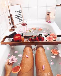 two people sitting in a bathtub with fruit on the floor and petals around them