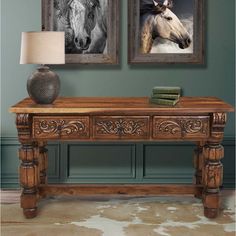 two framed horses are hanging on the wall above a wooden table with a lamp next to it