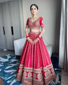 a woman in a red and gold lehenga standing on a blue carpet next to a white couch