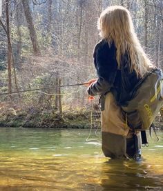 a woman is standing in the water holding a fishing rod and looking down at the river