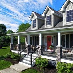 a house with white trim and black railings on the front porch, surrounded by greenery