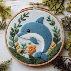 a blue dolphin with flowers and leaves on it's face is shown in an embroidery hoop