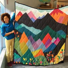 a woman standing next to a colorful quilt on a window sill with her arms in the air