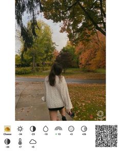 a woman walking down a sidewalk in front of trees with fall leaves on the ground