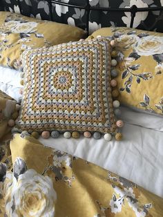 a crocheted pillow on top of a bed with yellow and white sheets,