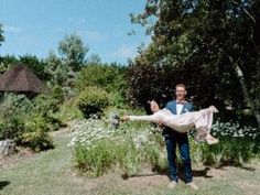 a man holding a woman in his arms while walking through a garden with white flowers