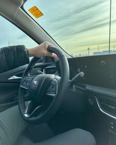 the driver's hand on the steering wheel of a car with a yellow sign in the background