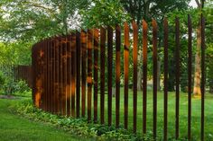 a large metal fence in the middle of a grassy area with trees and bushes behind it