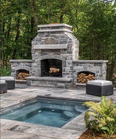 an outdoor fireplace with chairs around it and a pool in the foreground, surrounded by trees