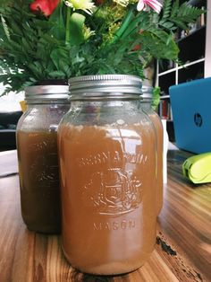 two jars filled with liquid sitting on top of a wooden table next to a plant