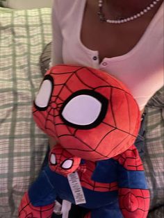 a spiderman stuffed animal sitting on top of a bed next to a person wearing a white shirt