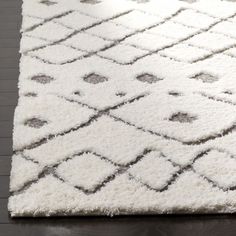 a white and gray rug on top of a wooden floor with dark wood floors in the background