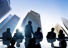 silhouettes of business people sitting at a table in front of tall buildings