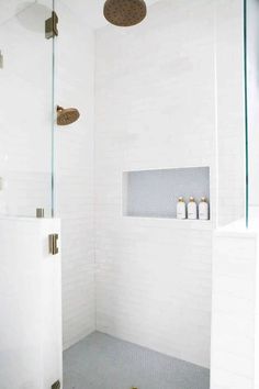 a bathroom with white tile and gold fixtures on the shower head, tub, and shelves