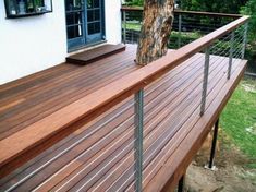 a wooden deck next to a tree in front of a house