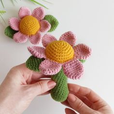 two crocheted flowers being held by someone's hand on a white surface