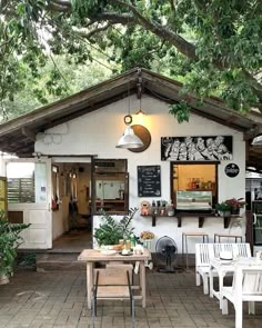 the outside of a small restaurant with tables and chairs under a large leafy tree