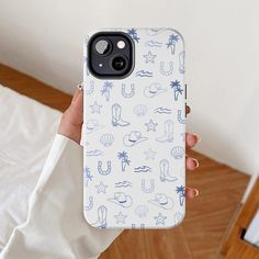 a person holding up a phone case with blue and white designs on it in front of a bed