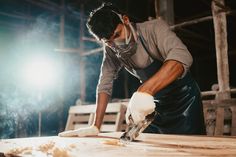 a man is working with wood in a workshop at night, wearing gloves and safety gear