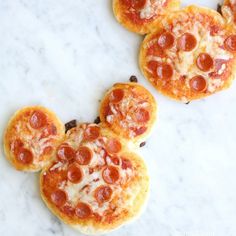 three mini pizzas shaped like mickey mouse heads on a white marble surface with chocolate chips