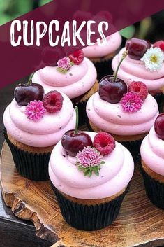 cupcakes with pink frosting, cherries and flowers on a wooden plate