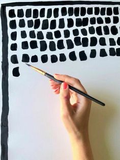 a person is holding a paintbrush in front of a piece of paper with black squares on it